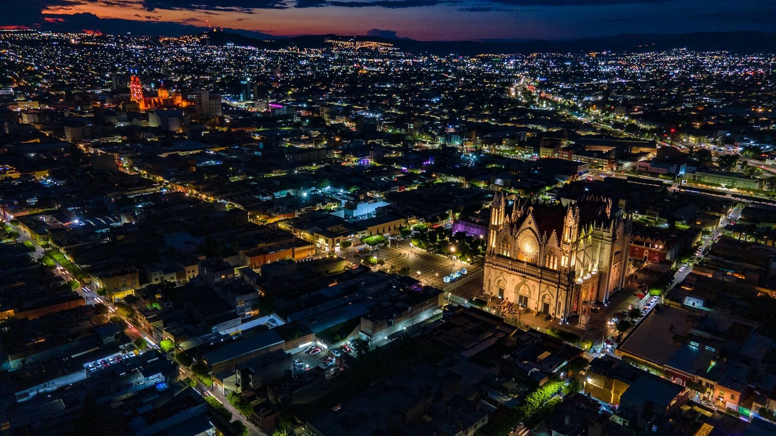 Stunning aerial view of a Mexican cityscape at night with illuminated cathedral and city lights.