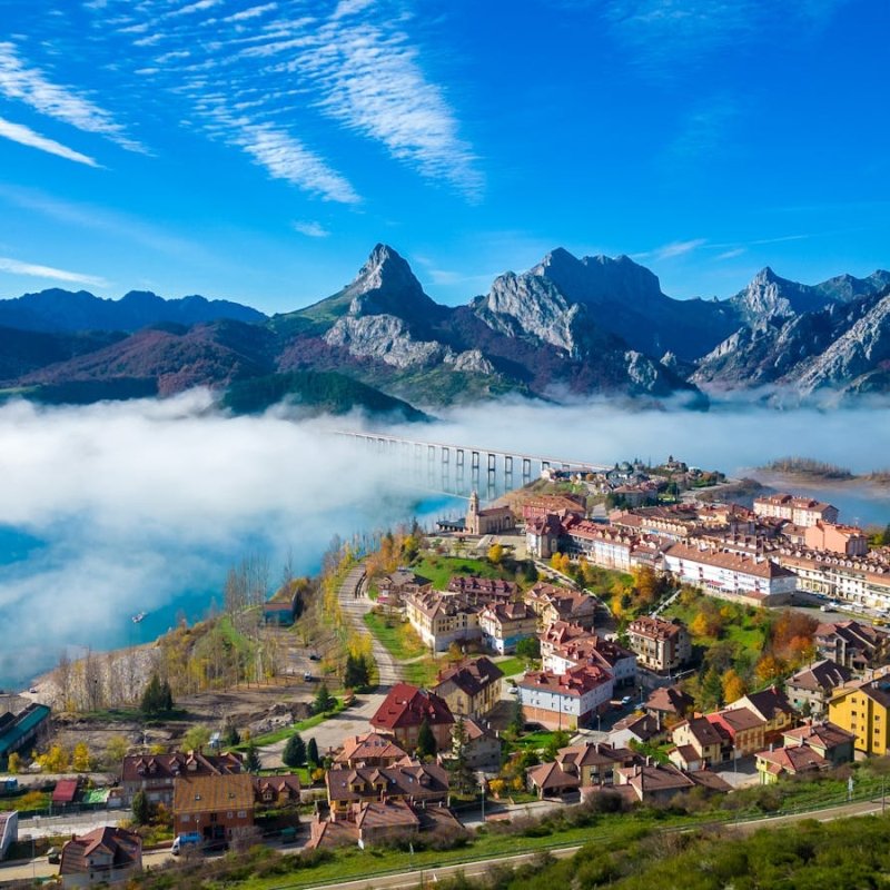 Captivating aerial view of Riaño, Spain with mist over the mountains and vibrant village colors.